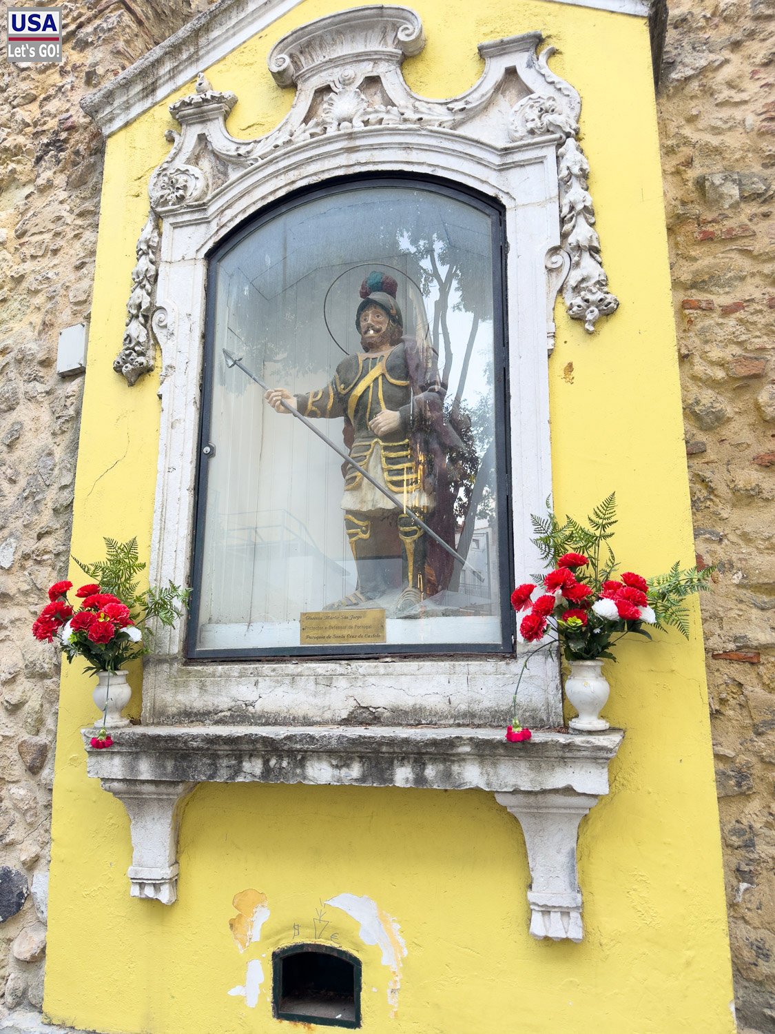 Heiligenfigur in einer Nische an einer gelben Hauswand