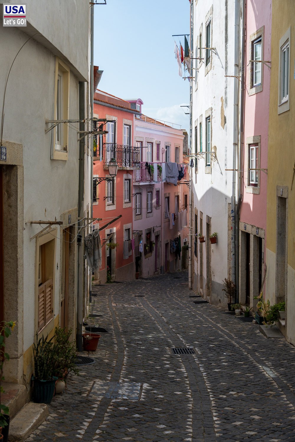 Gasse mit pastellfarbenen Häusern und Blumentöpfen in der Alfama