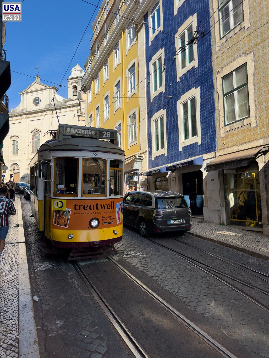Gelbe Straßenbahn vor bunten Häusern in einer Altstadtgasse
