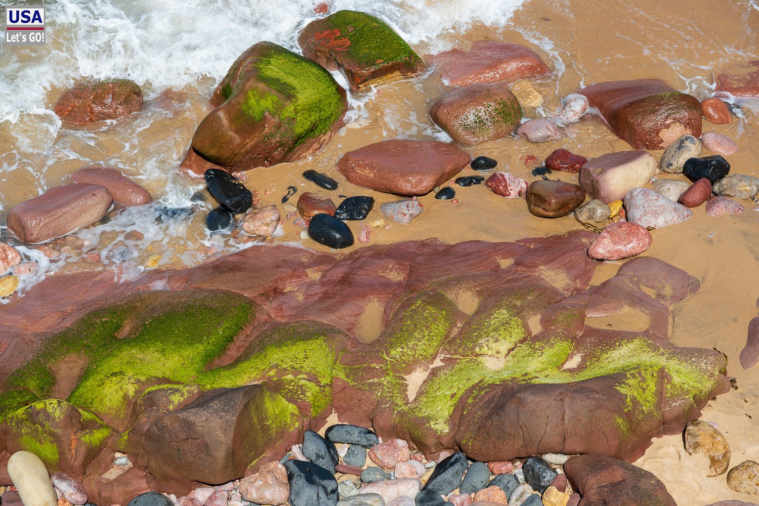 Bunte Kiesel und grün bemooste Felsen am Wasser